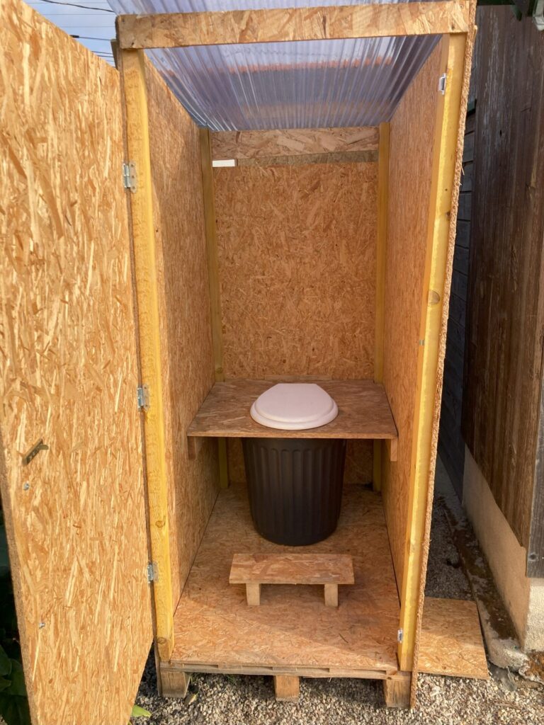Intérieur d’une toilette sèche artisanale avec assise en bois et bac de récupération, conçue pour la location d’événements écologiques à Rennes.