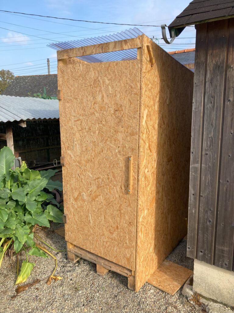 Toilette sèche en bois OSB avec toit en polycarbonate, posée sur une palette, idéale pour événements et locations à Rennes. Vue extérieure fermée.